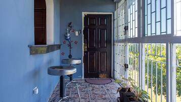 Un couloir avec un mur bleu, une porte en bois foncé et une fenêtre ornée d’un garde-corps en métal. On y trouve deux tabourets de bar et une plante en pot près de la porte.