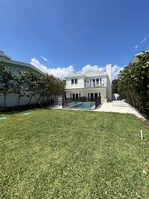 A modern two-story house with a swimming pool, surrounded by a well-maintained lawn and trees.