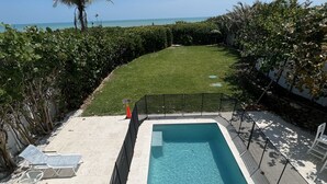 A rectangular swimming pool with a clear blue water, surrounded by a black fence, and a grassy area with a view of the ocean. - Steps to your own private beach (Vero Beach)