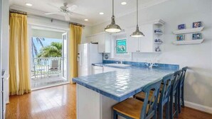 A kitchen with a blue island, white cabinets, and a ceiling fan. There are shelves with decorative items on the wall. - Steps to your own private beach (Vero Beach)