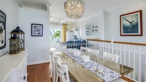 A dining area with a glass table, white chairs, a chandelier, and a view of the kitchen and outdoor space. - Steps to your own private beach (Vero Beach)