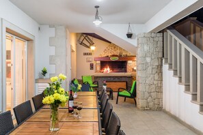Ein Essbereich mit einem Holztisch, Stühlen und einer Blumenvase. Im Hintergrund befindet sich ein Kamin und eine Treppe.
