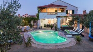 Una casa de dos pisos con piscina, mobiliario de exterior y un balcón.