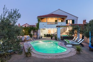 Une maison à deux étages avec une piscine, un espace salon extérieur et un balcon.
