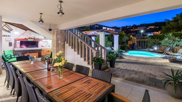 Un área de comedor al aire libre con mesa y sillas de madera, una parrilla y una piscina.