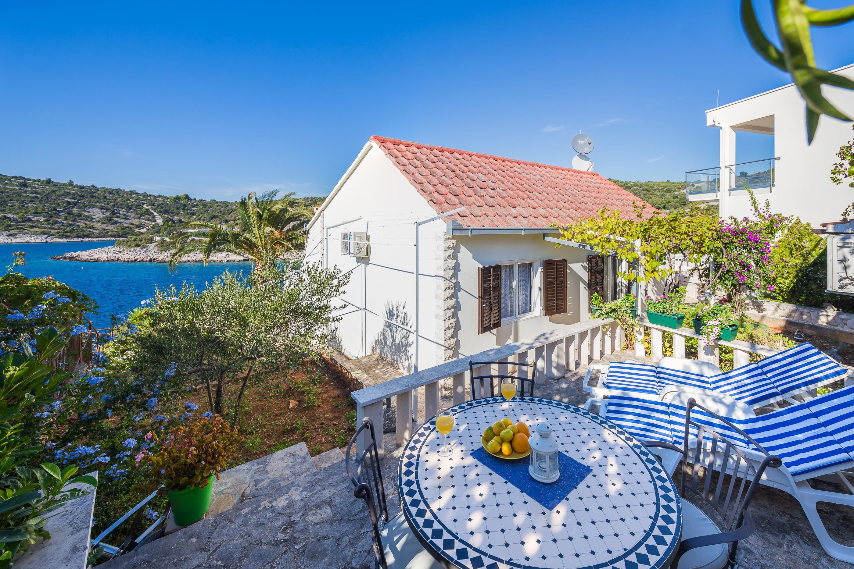 Eine Strandvilla mit einer gefliesten Terrasse, einem runden Tisch mit Obstschale und Meerblick.