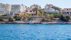 A coastal residential area with buildings, a stone wall, and a calm sea. - Cozy apartment  Bose 2+2 only 5 metres from the beach special discount -30%! (Dvornica, Rogoznica)