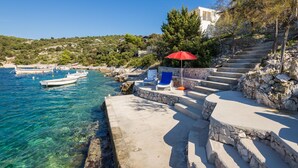 A coastal scene with clear blue water, a boat docked near the shore, and a staircase leading down to the beach. - Cozy apartment  Bose 2+2 only 5 metres from the beach special discount -30%! (Dvornica, Rogoznica)