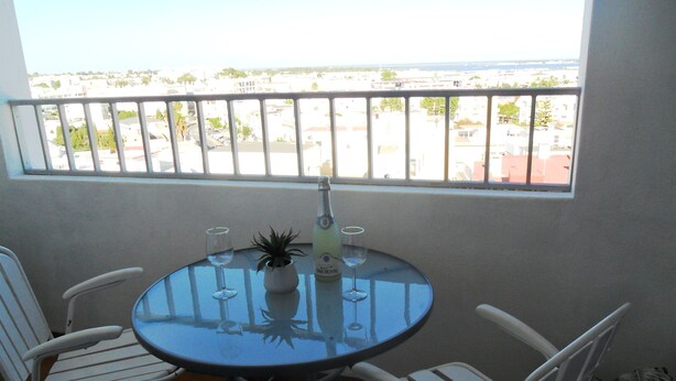 A round table with two white chairs, a bottle of champagne, and two wine glasses on a balcony with a view of a cityscape. - A Beautiful Home with a View in Olhao, Algarve (Olhao)