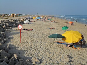 Een strand met mensen die zonnebaden en zwemmen, een verbodsbord voor zwemmen, en parasols.