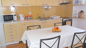 A compact kitchen with wooden cabinets, a microwave, a sink, and a stove. There is a dining table with chairs and a fruit basket on it. - A Beautiful Home with a View in Olhao, Algarve (Olhao)