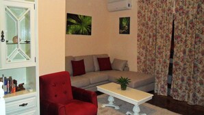 A living room with a red armchair, a beige sofa, a white coffee table, and floral curtains. - A Beautiful Home with a View in Olhao, Algarve (Olhao)