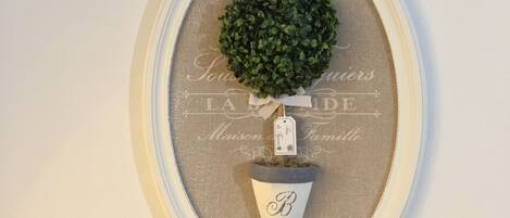 Decoración de pared en marco con una planta pequeña en maceta, una etiqueta y una placa de identificación.