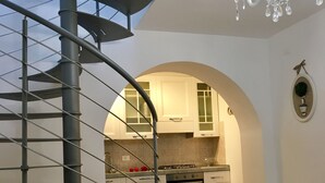 Une cuisine moderne avec des armoires blanches, un four encastré et un escalier en colimaçon menant à un niveau supérieur.