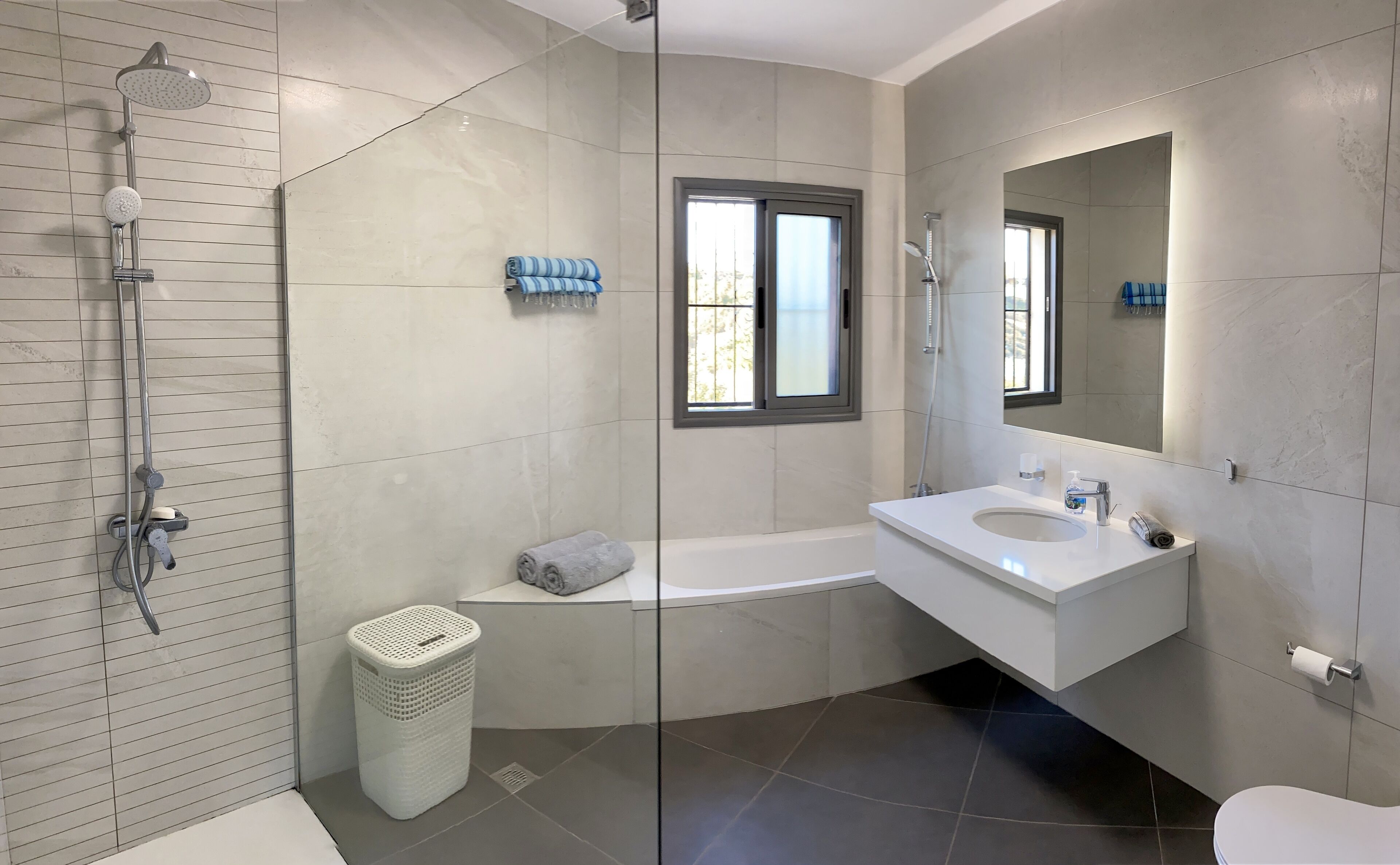 Une salle de bain moderne avec une douche à parois de verre, une baignoire, un lavabo blanc et un grand miroir.