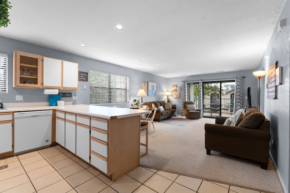 A modern kitchen with a central island, a dining area with a table and chairs, a sofa, and a large sliding glass door leading to an outdoor patio.