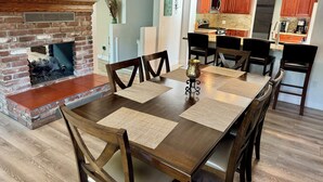 Un comedor con chimenea de ladrillo, sillas de madera y una mesa con individuales.