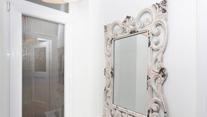 Un baño con una puerta blanca, una ventana con vidrio esmerilado y un espejo decorativo con diseños elaborados.