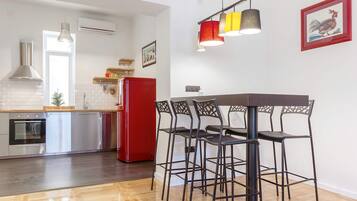 A modern kitchen with a red refrigerator, a dining table with chairs, and a hanging light fixture.