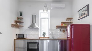 Una cocina moderna con electrodomésticos de acero inoxidable, estantes de madera y un refrigerador rojo.