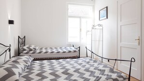Un dormitorio con una cama grande, otra más pequeña, una ventana y una puerta.