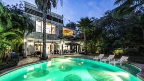 Un resort moderno con piscina, mobiliario de exterior y abundante vegetación.