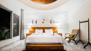 Un dormitorio moderno con techo de ladrillo curvo, una cama grande con ropa blanca, una mesita de noche con lámpara, una silla de madera y un tocador.