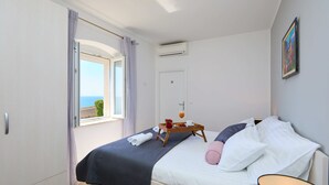 Quarto com cama, mesa de cabeceira com bandeja de café da manhã, janela com cortinas e ar-condicionado.