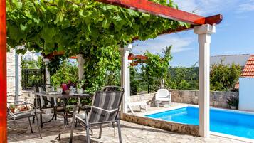 Relax in a serene outdoor setting with a pool, lush greenery, and comfortable seating.