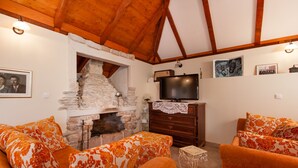 A cozy living room with a stone fireplace, wooden beams, a television, and floral-patterned sofas. - Countryside Family Villa with Private Pool (Donje Selo)