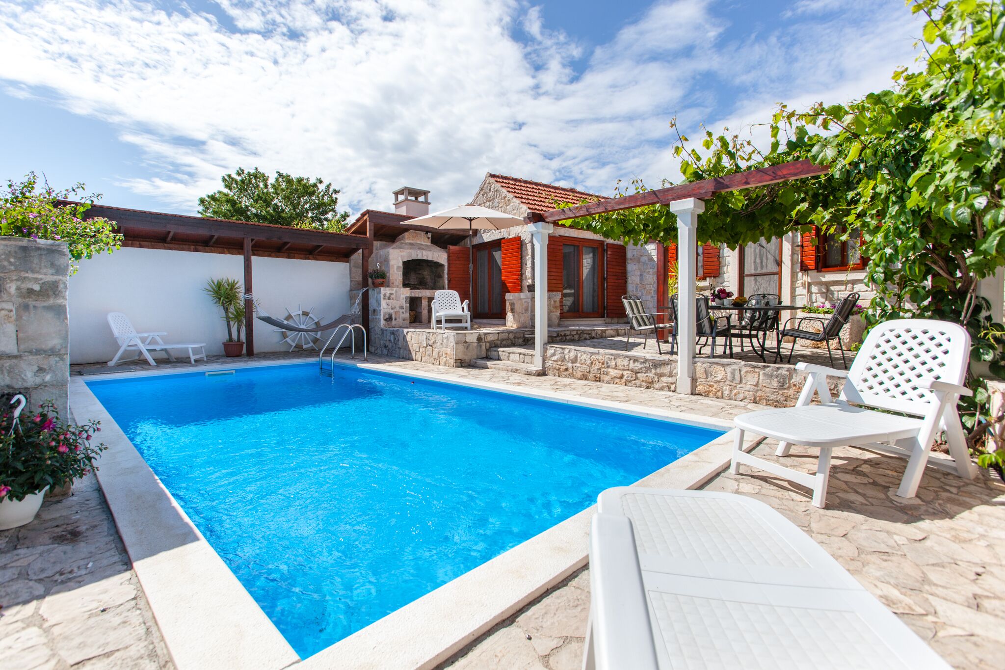 A swimming pool with lounge chairs and a pergola, surrounded by stone walls and vegetation.