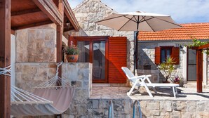 A stone building with a wooden door, a hammock, a white lounge chair, and a patio umbrella. - Countryside Family Villa with Private Pool (Donje Selo)
