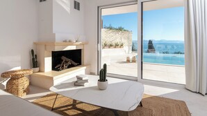Un salon moderne doté d’une cheminée, d’une grande fenêtre offrant une vue sur une piscine et des montagnes, et d’un balcon avec un mur en pierre.