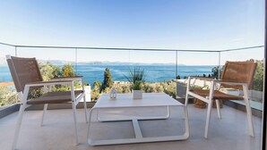 Un balcon avec deux fauteuils en osier et une petite table, offrant une vue panoramique sur la mer et les montagnes lointaines.