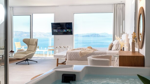 Une chambre d’hôtel moderne dotée d’une grande fenêtre, d’un lit, d’un canapé, d’une télévision et d’un jacuzzi.