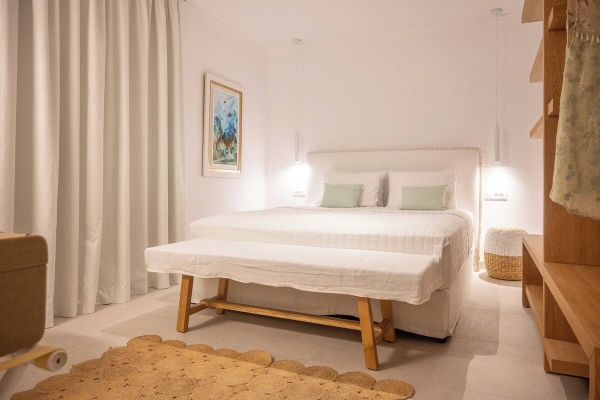 A bedroom with a bed, bedside lamps, a woven rug, and a painting on the wall.