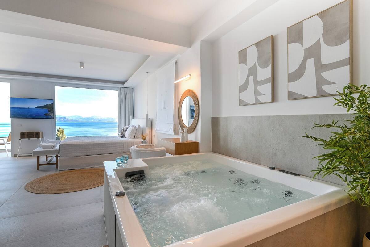 A modern hotel room with a large bathtub, a sofa, a TV, and a view of the sea.