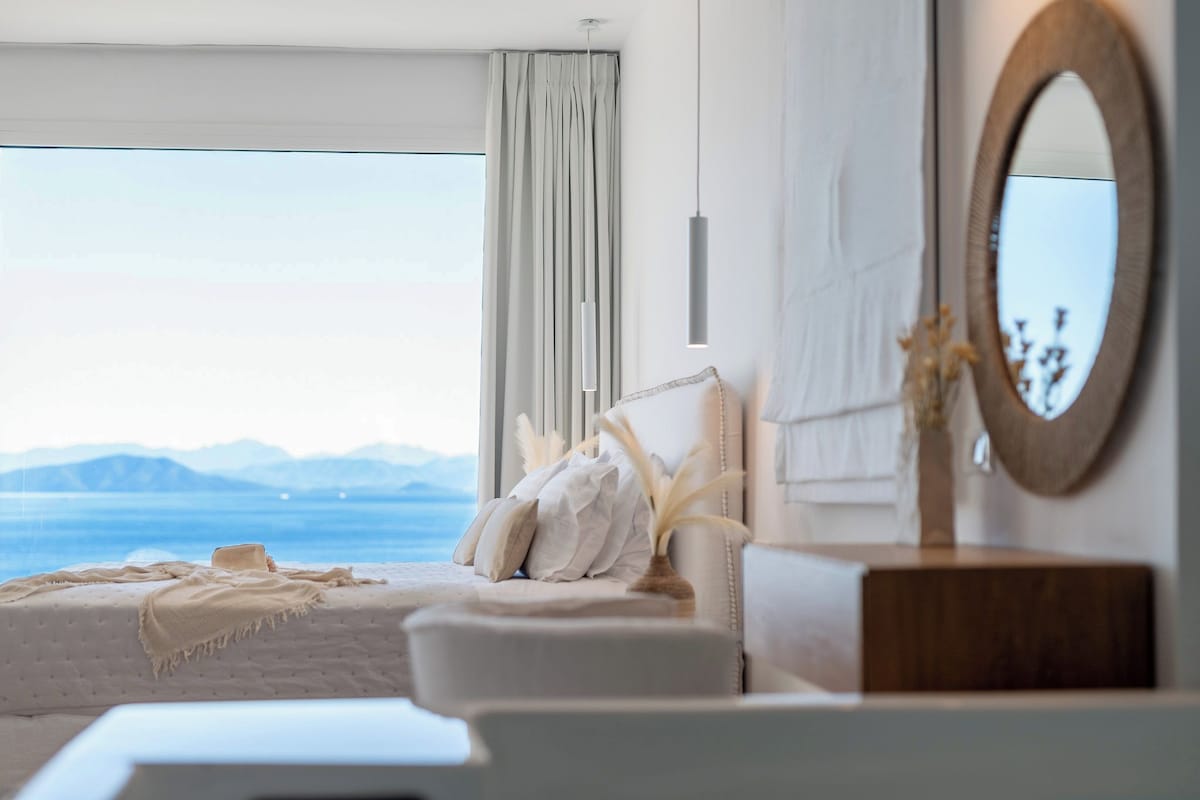 Un dormitorio con una ventana grande, una cama, una mesita de noche y un espejo.