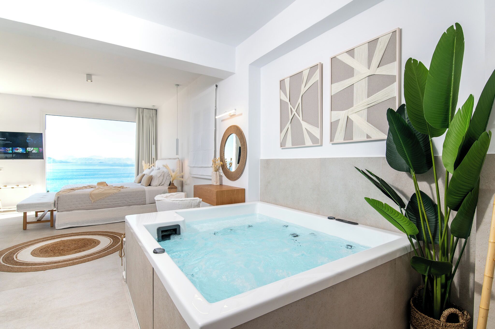 Ein modernes Hotelzimmer mit großem Fenster, einem Bett, einer Sitzecke, einer Badewanne und Blick auf den Ozean.