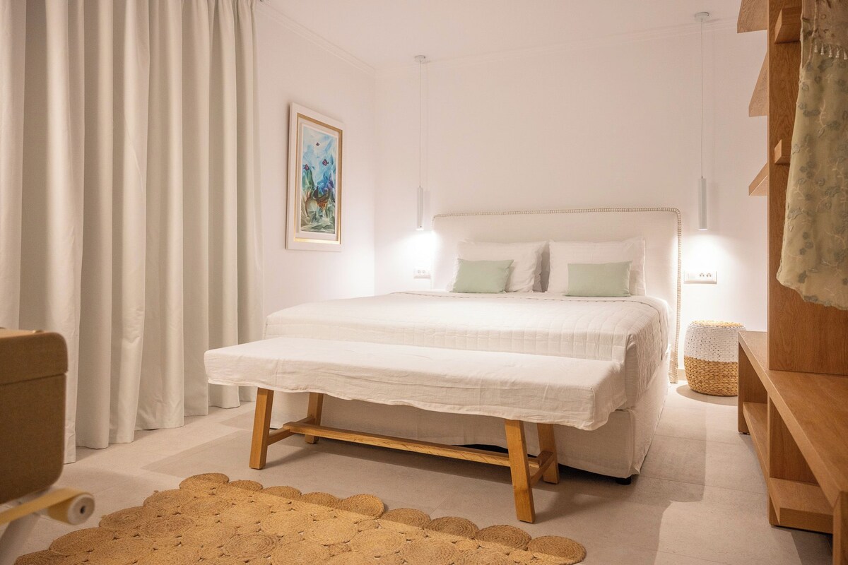 A bedroom with a bed, bedside lamps, a woven rug, and a painting on the wall.