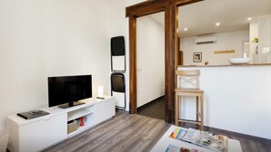 Un salón moderno con televisor de pantalla plana, un mueble blanco para equipo multimedia y una mesa de comedor de madera con revistas.