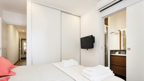 Habitación de hotel con cama, televisión montada en la pared y baño visible a través de una puerta abierta.