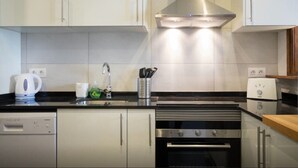 Una cocina moderna con gabinetes blancos, una campana extractora de acero inoxidable, un lavavajillas y un horno.