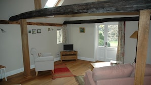 A cozy living room with wooden beams, a white sofa, a pink sofa, a wooden TV stand, and a red rug. - Converted Granary in SE Kent UK (Lyminge, nr Folkestone)