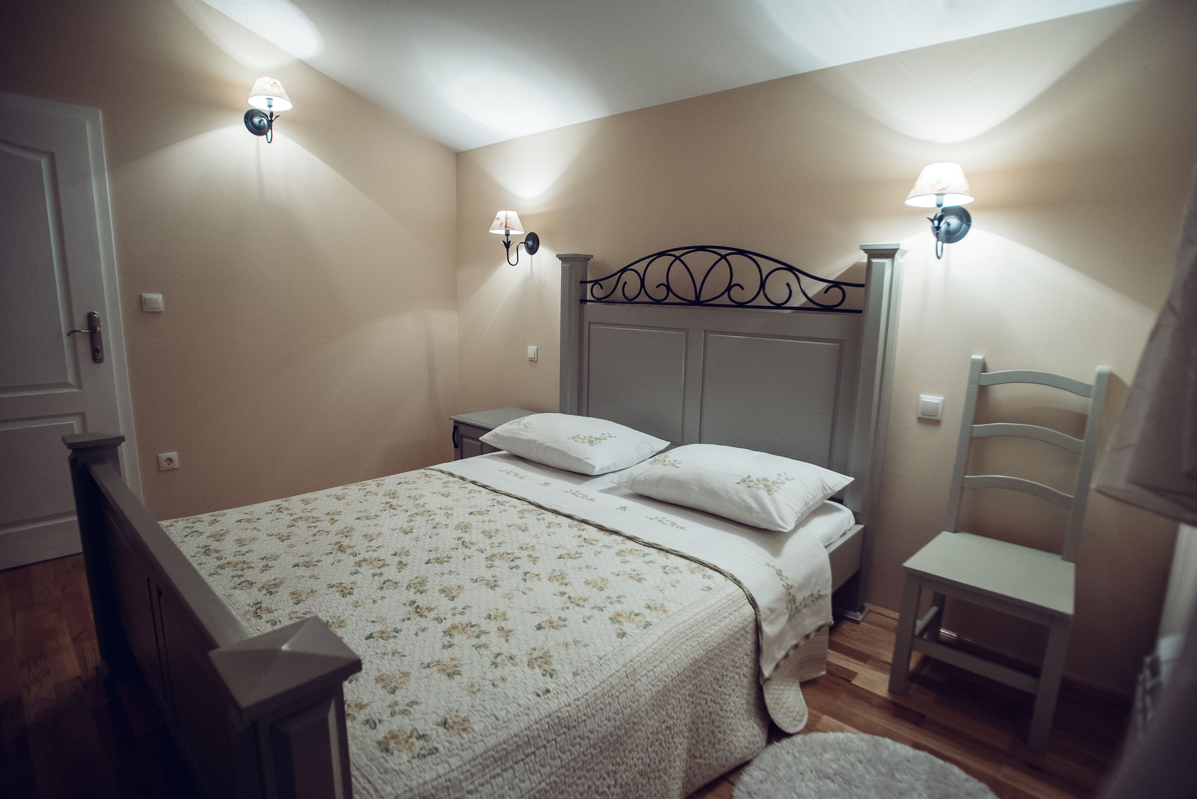 A bedroom with a bed, nightstands, a chair, and wall-mounted lamps.