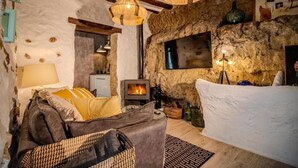 A rustic interior with a stone wall, a fireplace, a sofa, and a dining area. - Cave Suite THA (Cave Hotel Lomas de Ruvira) (Jorquera)