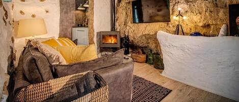A rustic interior with a stone wall, a fireplace, a sofa, and a dining area.