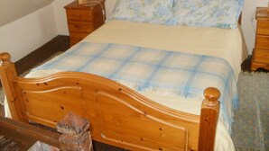 Een houten bed met een geruit sprei, twee nachtkastjes met lampen en een nachtkastje van hout.