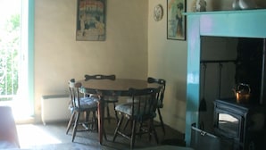 Een rustieke eethoek met een houten tafel en stoelen, een hanglamp en een open haard met een klok erboven.