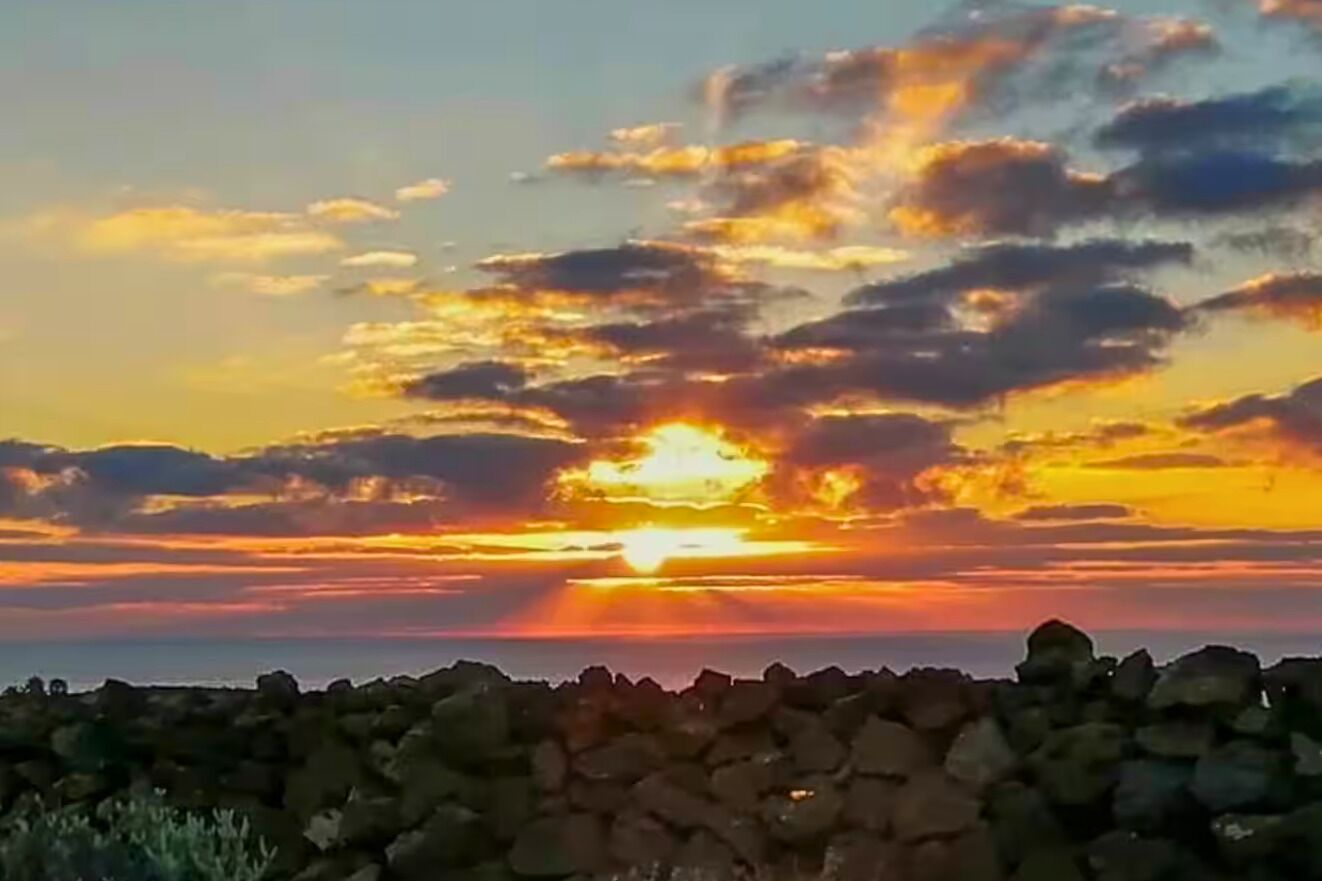 A sunset over a rocky shoreline with a stone wall in the foreground.